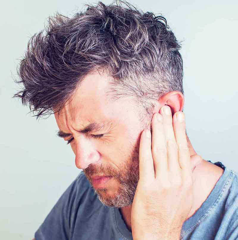 Man holding his ear trying to stop the ringing in his ear he is experiencing.